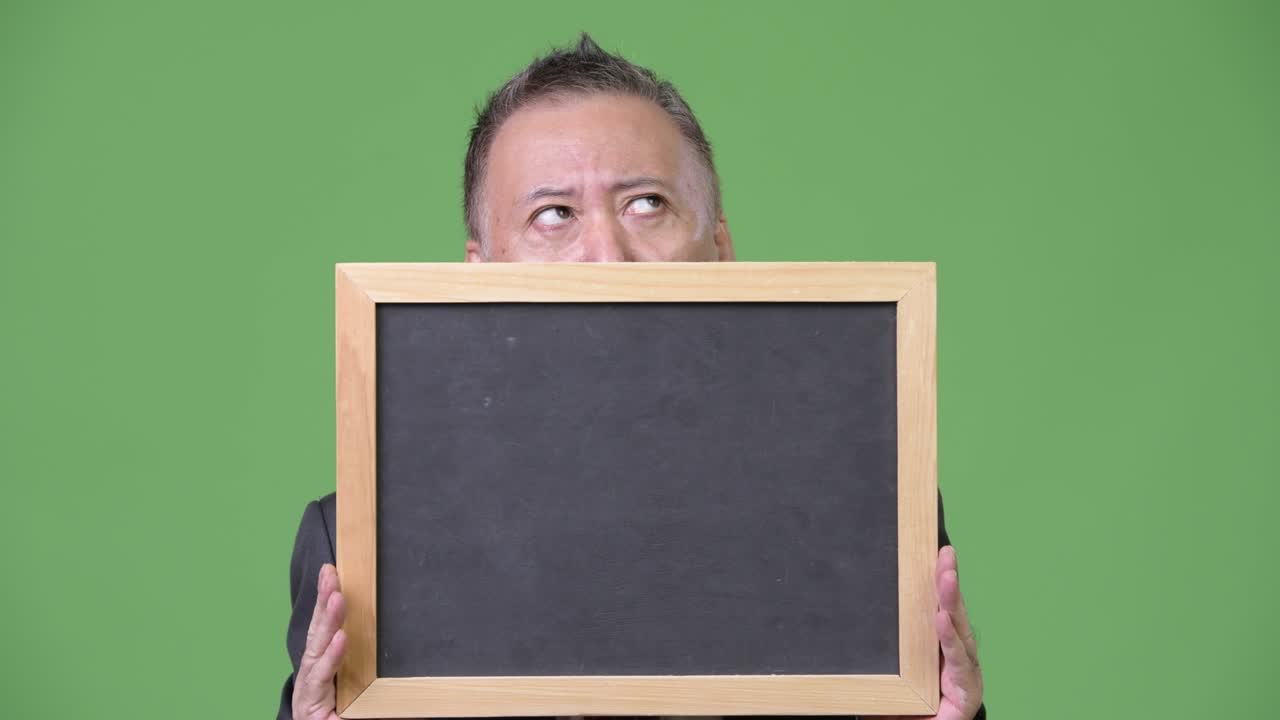 성숙 한 일본인 사업가 가 초록색 배경 에 검은판 을 들고 있다