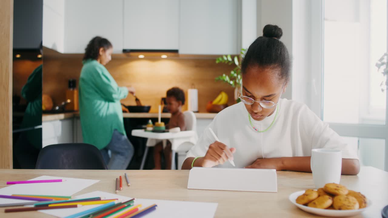 Teenage Girl Drawing on Tablet in Kitchen while Family Eats Dinner