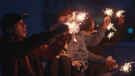 Fröhliche-Freunde-Halten-Wunderkerzen-In-Der-Hand-Und-Feiern-Silvester-Auf-Dem-Dach-Bei-Sonnenuntergang-Und-Haben-Spaß-Daran,-Die-Feiertagsfeier-Zu-Genießen