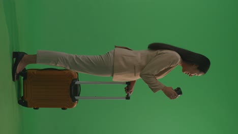 businesswoman looking at camera while carrying suitcase on green screen