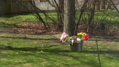 A-pot-of-fake-flowers-hangs-on-a-shepard's-hook,-moving-lightly-in-the-summer-wind