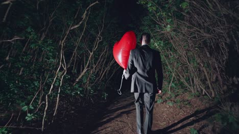 solitary businessman walking away through dark forest at night, carrying large red heart shaped balloon, symbolizing emotional journey of love, loss, and introspective solitude