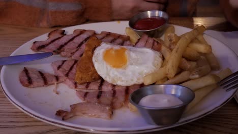 a hearty plate of grilled gammon, fried egg, chips, and dipping sauces indoors