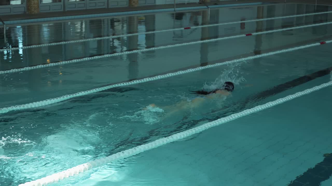 A serene image capturing a female figure swimming leisurely in an enclosed pool area with natural light casting over the water