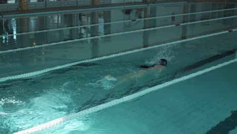 a serene image capturing a female figure swimming leisurely in an enclosed pool area with natural light casting over the water