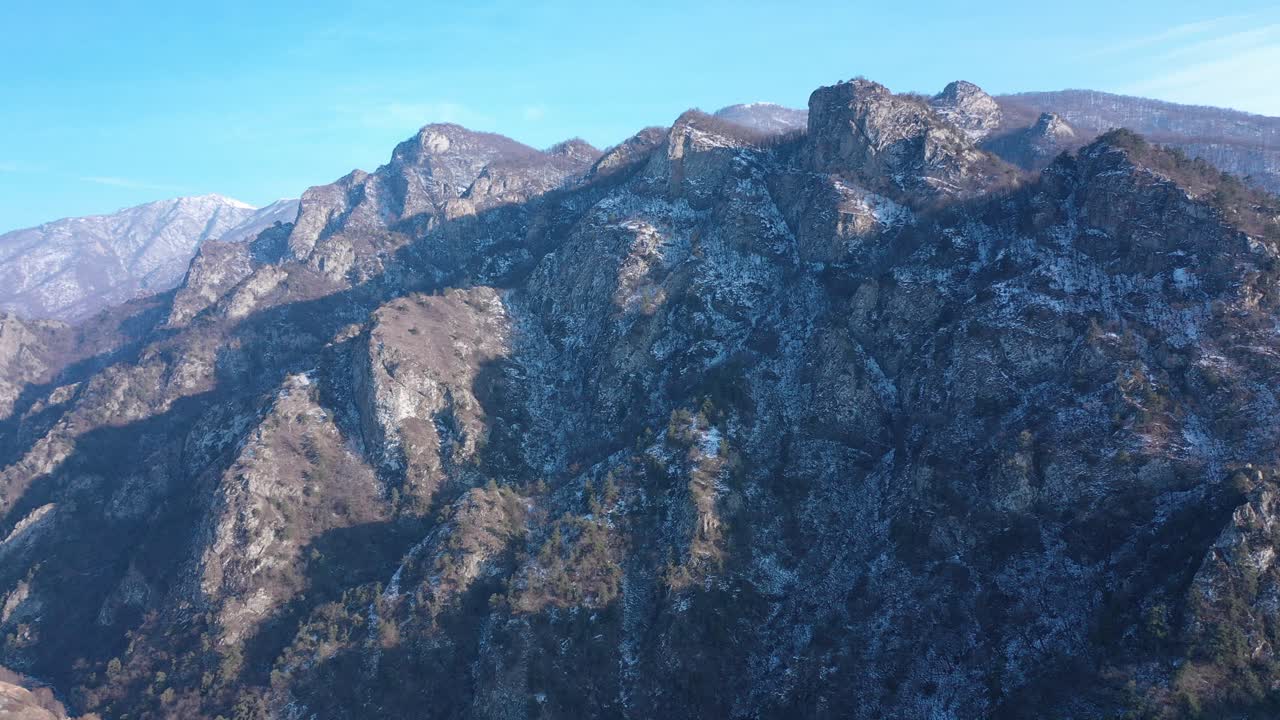 High alpine mountain road cuts across rugged slopes with exposed rock, steep terrain, and dramatic elevation changes