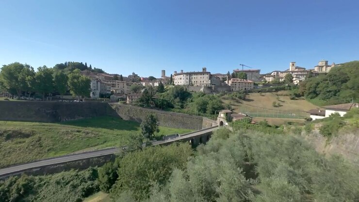 Un volo di drone aereo che sorvola rigogliosi vigneti verdi e ulivi verso le storiche mura in pietra e il maestoso skyline di Bergamo Città Alta
