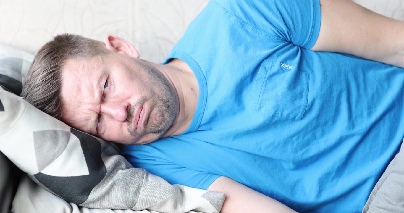 Upset man covers head with pillow creating sleep frustration