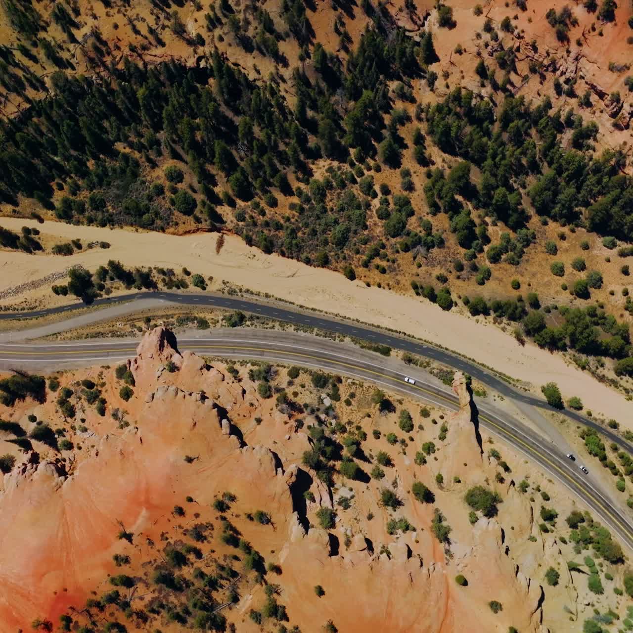 Lonely car travelling by the motorway through the National Arches Canyon Park. Aerial view on the sunlit landscape with pine trees growing on