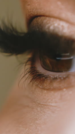 cu, slow motion: brown eyed young woman applies mascara on long artificial lashes with brush on blurred background extreme close side view