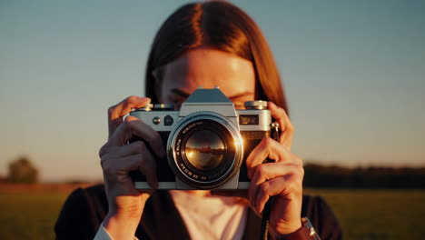 a woman takes a photograph with a vintage film camera at sunset
