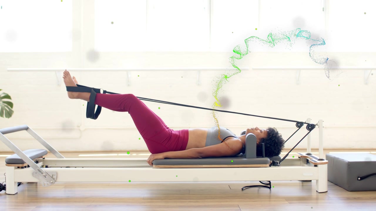 Donna che pratica Pilates usando le cinghie del reformer, esegue una serie di esercizi per le gambe per il core con particelle che tracciano le gambe.