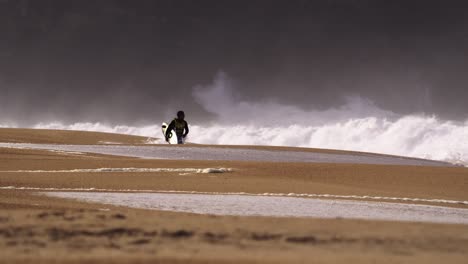 El-Hombre-Camina-En-Una-Playa-Vacía-En-Traje-De-Neopreno-Que-Lleva-Una-Tabla-De-Surf