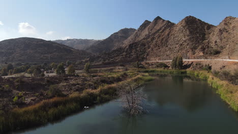 A-drone-chasing-birds-flying-over-a-river-winding-past-a-mountain