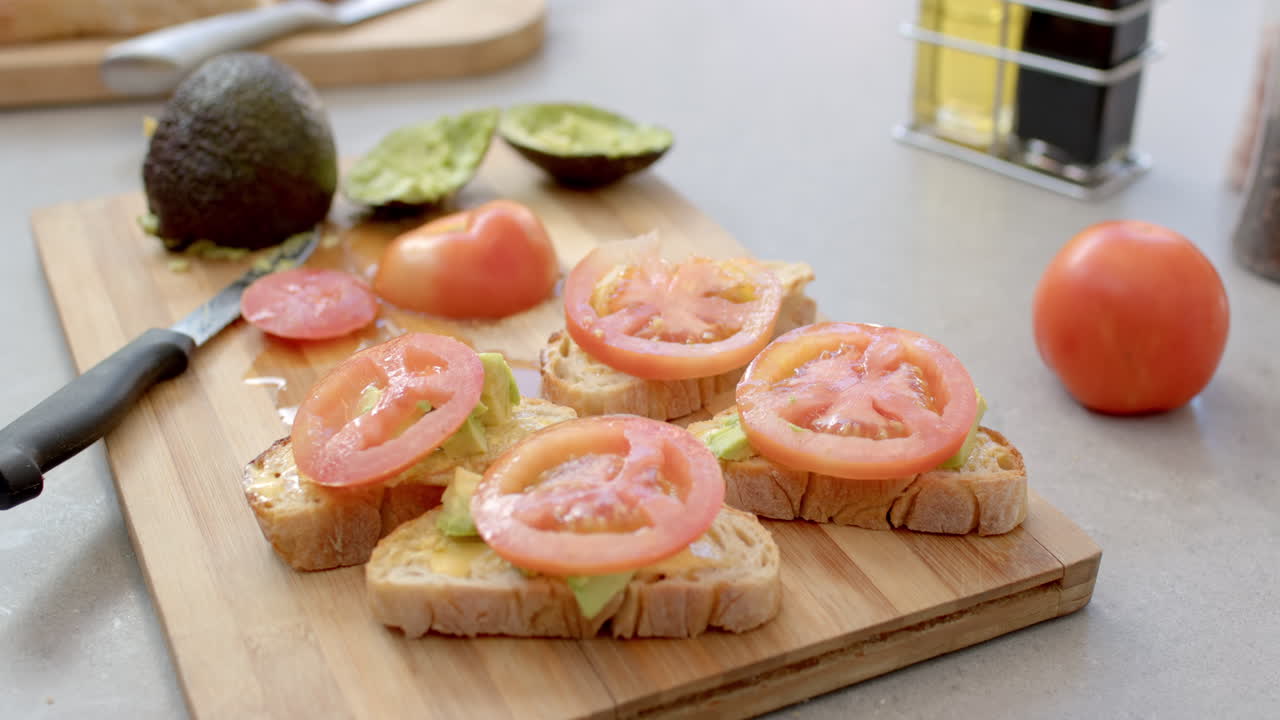 Preparing avocado toast with tomato slices on wooden cutting board in kitchen