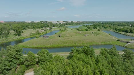 Aerial-establishing-view-of-abandoned-historical-concrete-seaside-fortification-buildings,-Southern-Forts-near-the-beach-of-Baltic-sea-in-Liepaja,-sunny-summer-day,-wide-drone-dolly-shot-moving-left