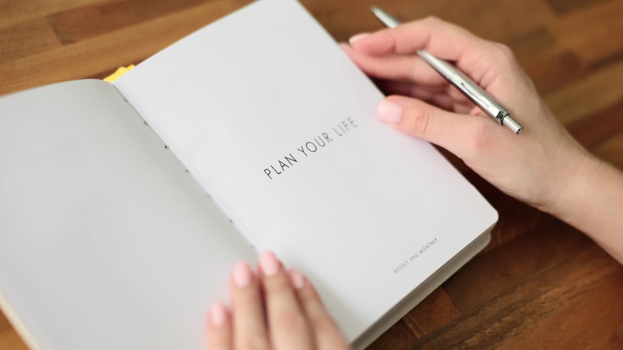 Woman opens white paper planner and writes down weekly plans