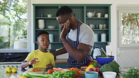 African-american-father-and-son-in-kitchen-wearing-aprons-and-preparing-dinner-together