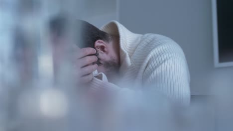 panorámica del hombre sentado a la mesa con las manos frotándose la cabeza