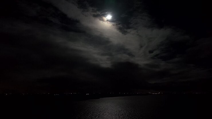 Illuminazione: luna piena tra le nuvole di notte. Il riflesso sul mare. Ampia ripresa aerea statica. Notte tranquilla e serena in America.