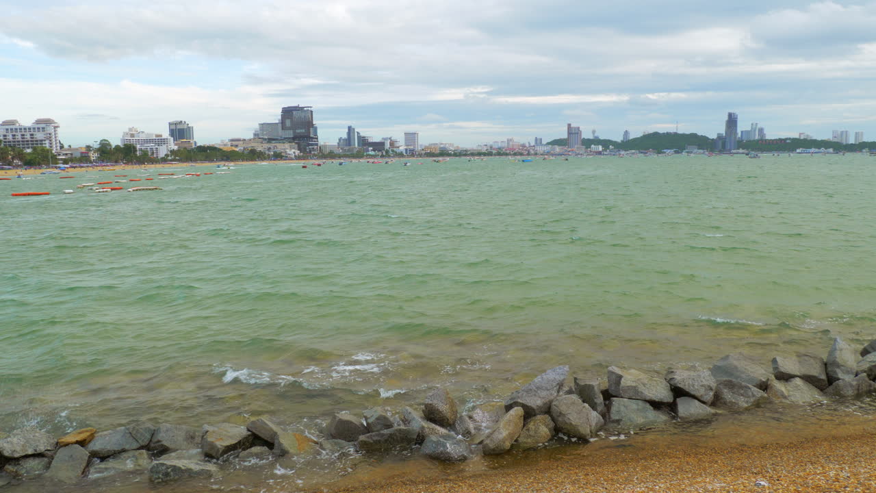 건물과 언덕에 둘러싸인 작은 파도가 있는 갈색 모래 해변과 물 위에 떠다니는