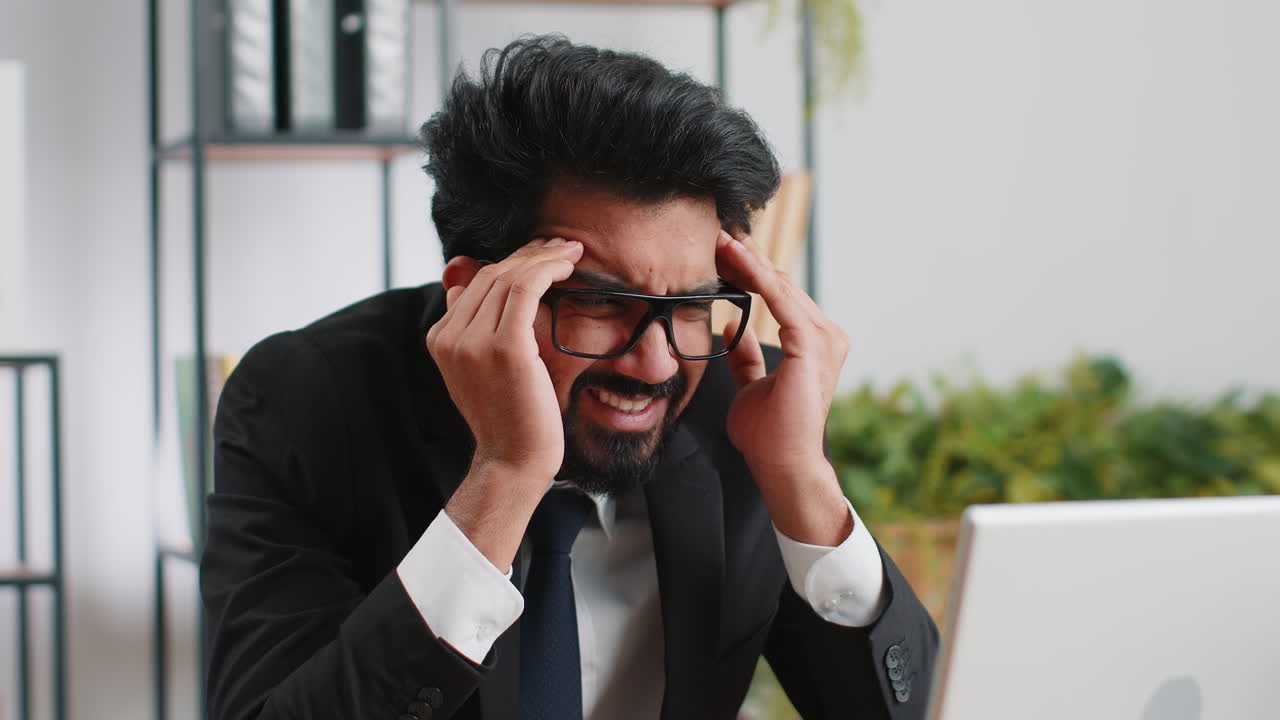 Tired indian business man suffering from headache problem tension migraine stress at home office
