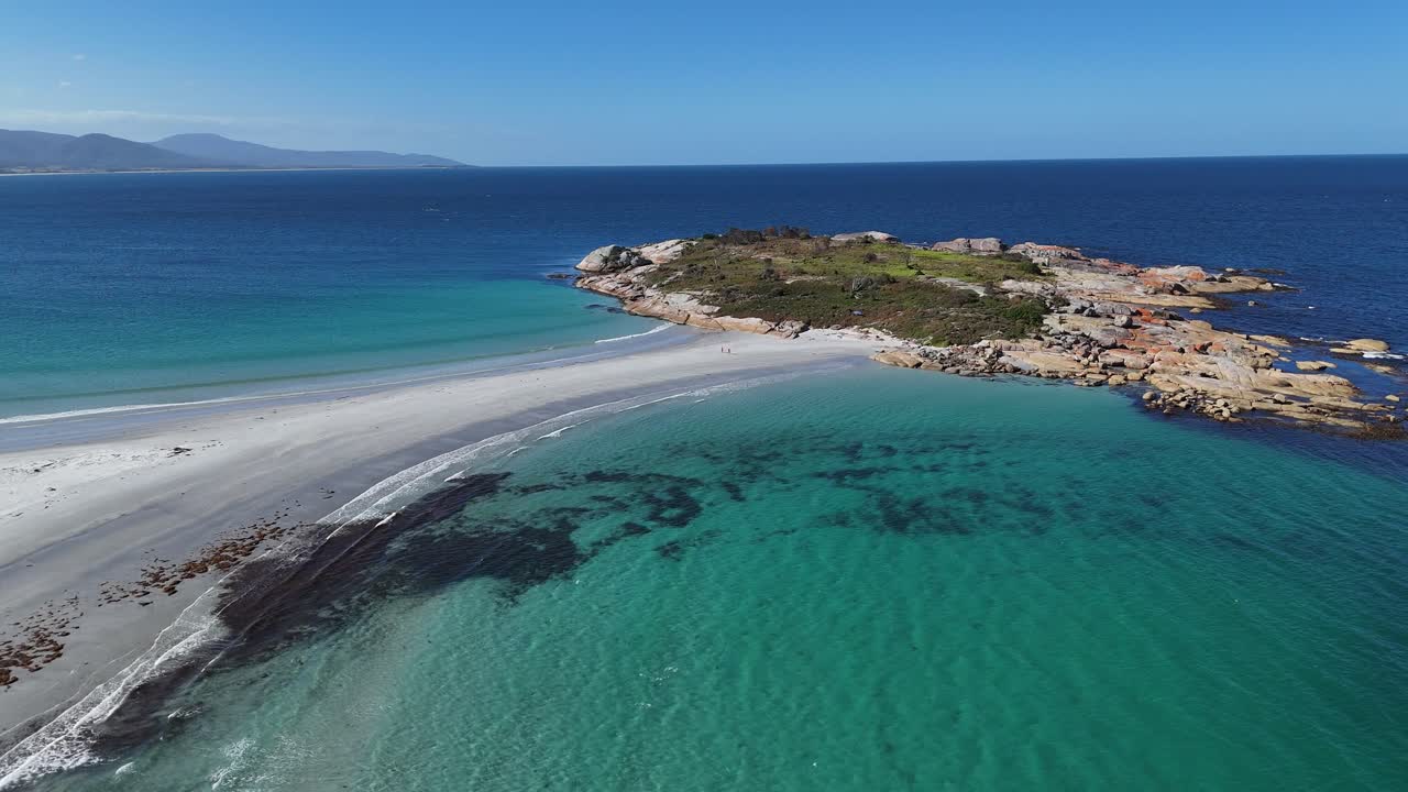 Small island with a sandbar with blue sea and turquoise waters, aerial shot rearward