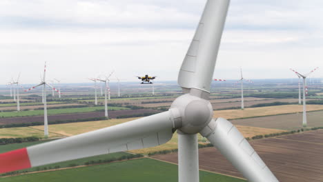 a drone flies amongst rotating wind turbines in an electricity generating farm, as it surveys and inspects the condition of the structures