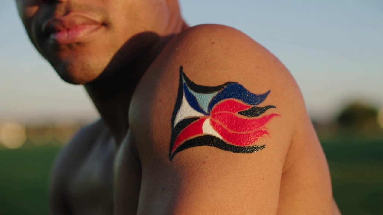 Camera starting shirtless man turning head and moving lips in park, showing glossy arm emblem
