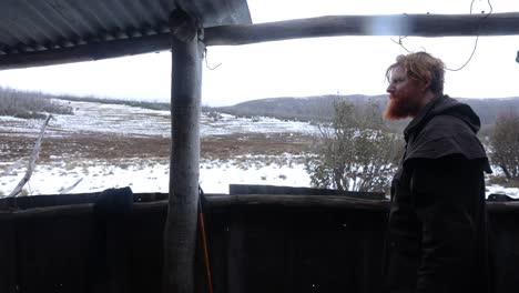 a traditional bushman looks out from the shelter of a high country hut to a snowy landscape in australia high country