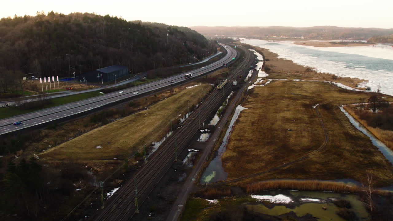 Aerial view of a highway, train tracks, and icy river landscape