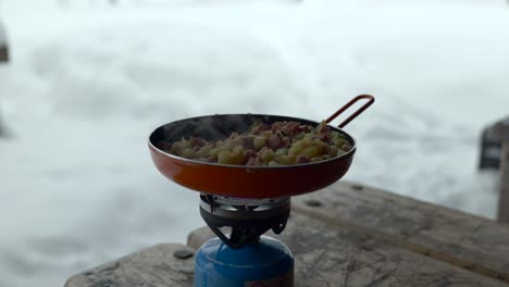 cooking food in a orange pan outdoors in a snowy landscape