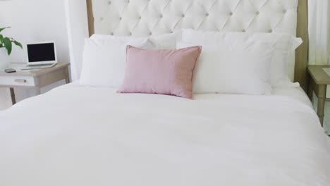 dormitorio blanco limpio con escritorio y portátil, gran cama blanca con almohadas blancas y grises.