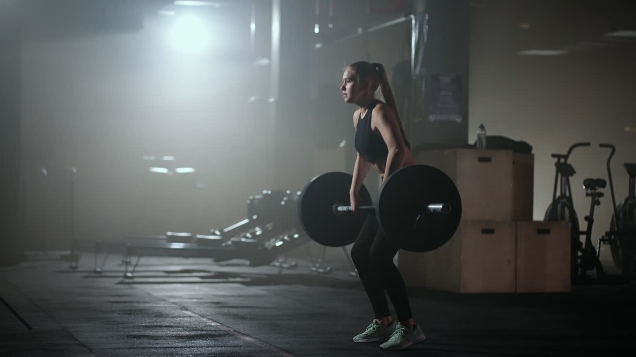 Female bodybuilder doing exercise with weights in gym. a female weightlifter performs a barbell lift in a dark gym. Female Bodybuilder Does Weight Lift Workout Exercises in the Hardcore Training