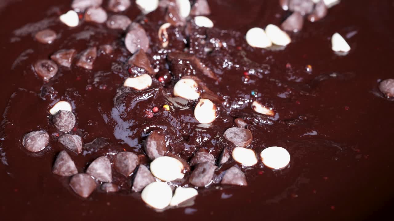 Spoon stirring melted chocolate with sprinkles and chocolate chips