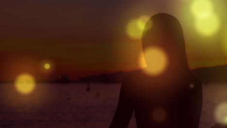 video generado digitalmente de manchas brillantes de color naranja que se mueven contra la silueta de una mujer que realiza yoga