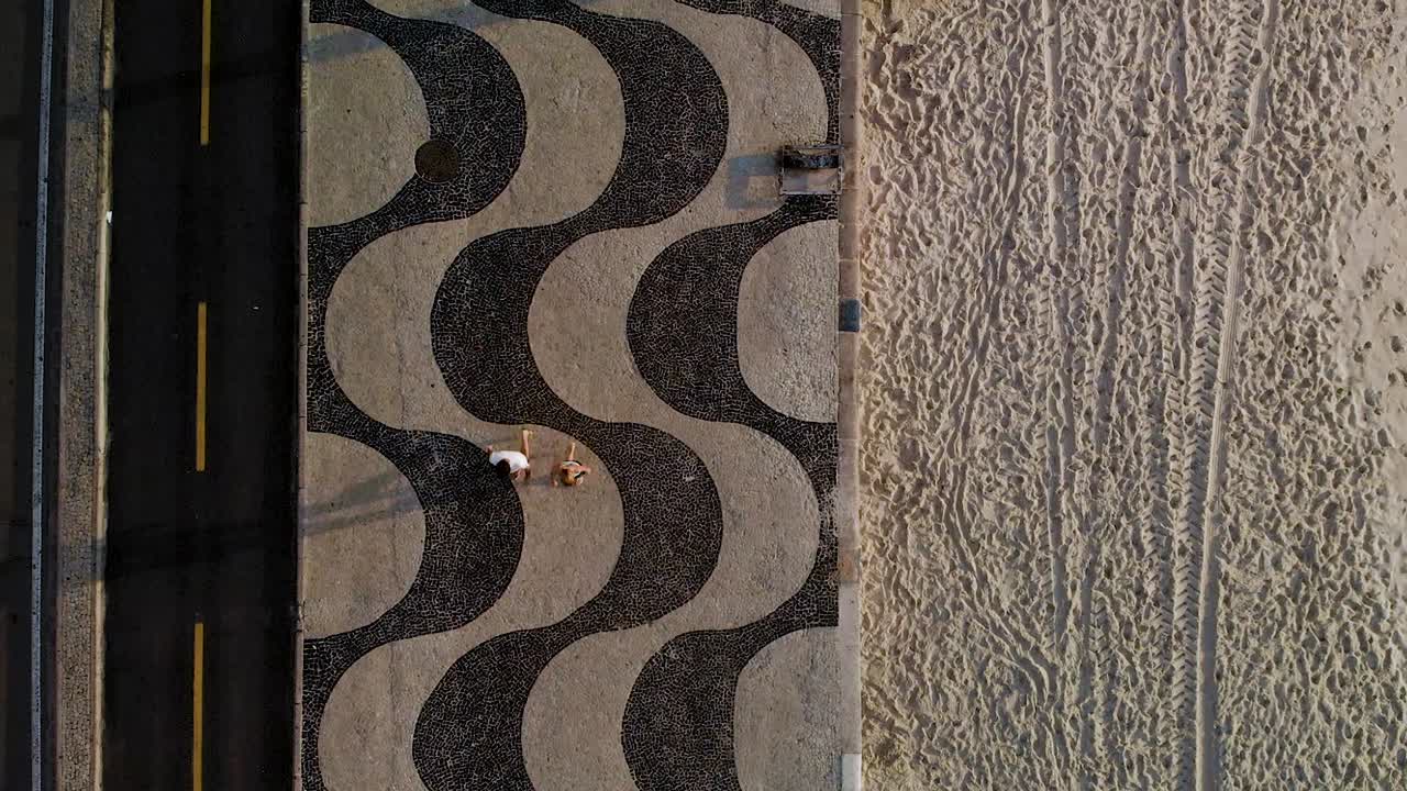 Top down aerial split view of Copacabana beach with patterns in the sand on the right and the pavement boulevard on the left
