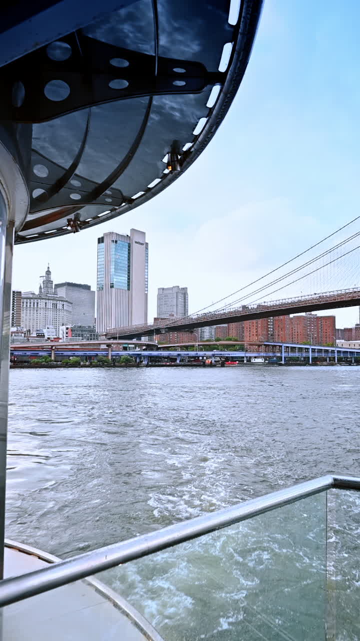 Watching the Manhattan Bridge against pink cloudscape from the boat travelling by the East River. Cruise around New York at sunset. Vertical video