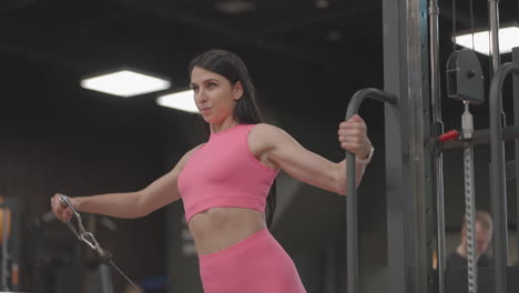 a young woman in a crossover raises her shoulder arms in a pink suit. exercises for training the arms and shoulders