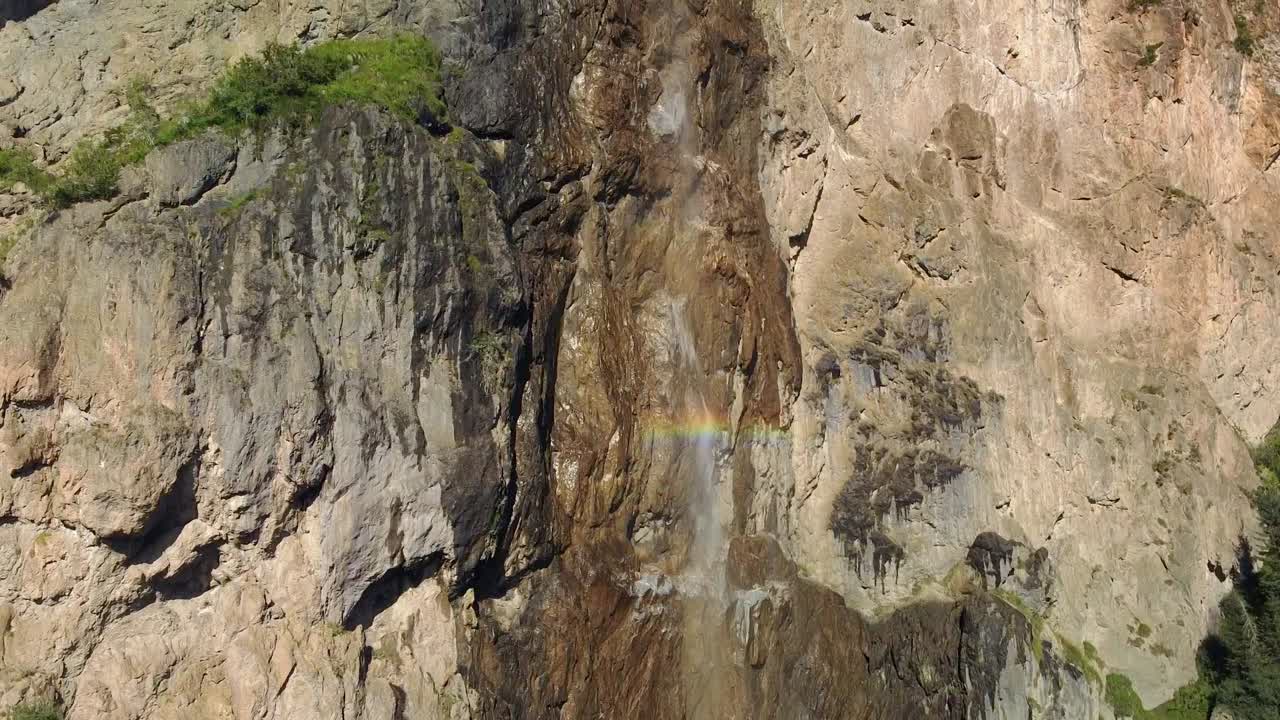 cascada alpina de la pared rocosa con colores del arco iris, toma aérea de abajo hacia arriba