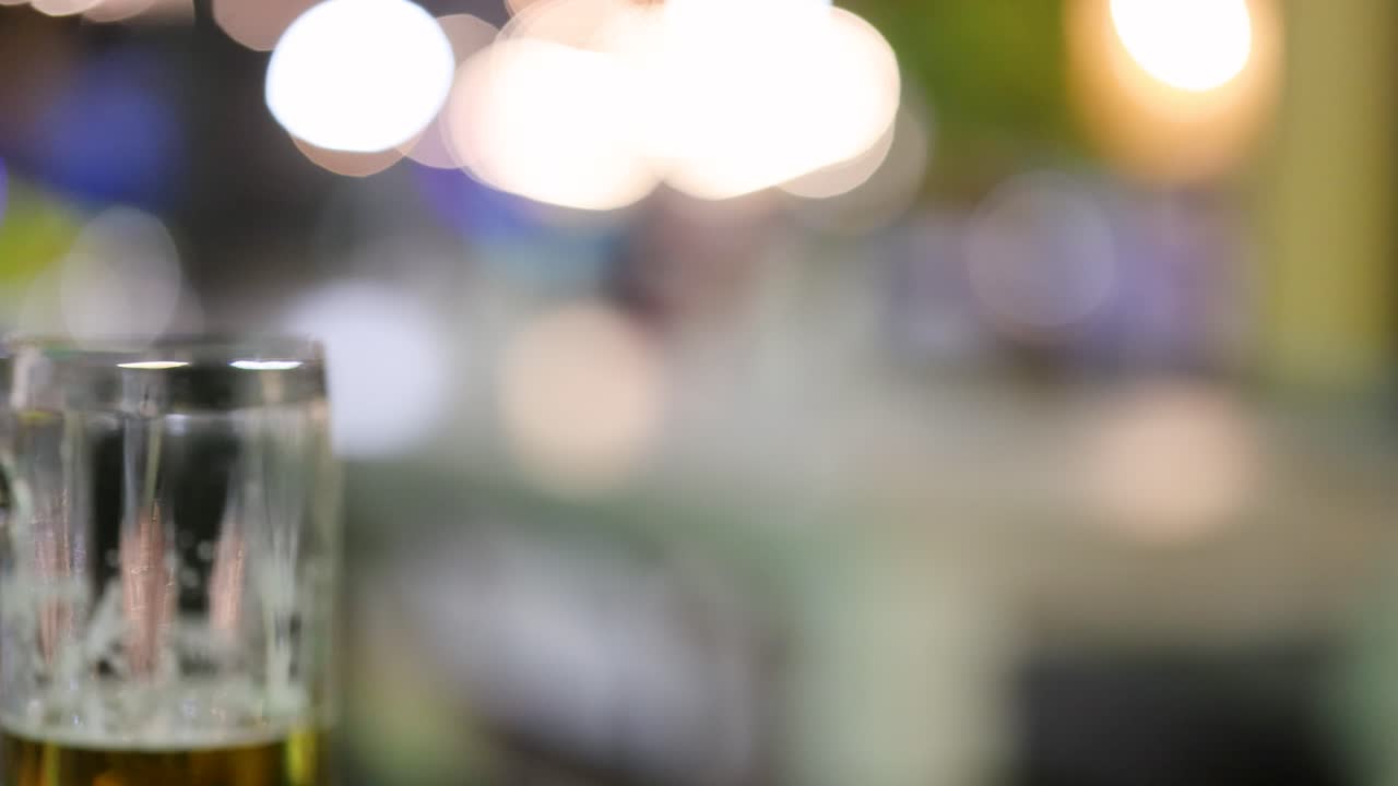 un vaso de cerveza en foco contra un fondo nocturno borroso y colorido, capturando una atmósfera animada y vibrante