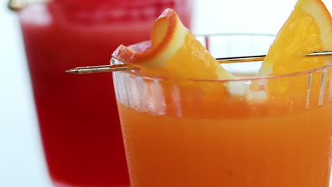 close-up of orange and red juices with citrus garnish in clear glasses.