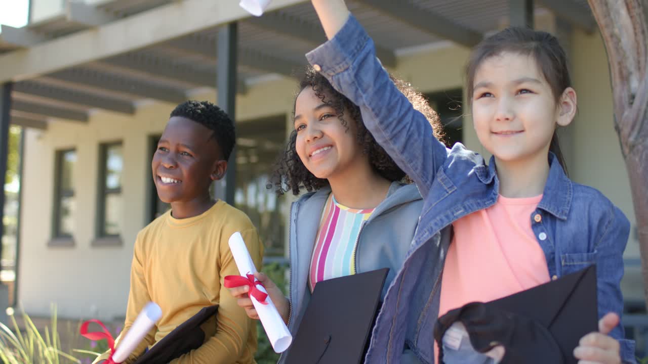 Diversi adolescenti che si filmano a scuola mentre mostrano i diplomi con un nastro rosso e lanciano in aria i cappelli per la cerimonia di diploma