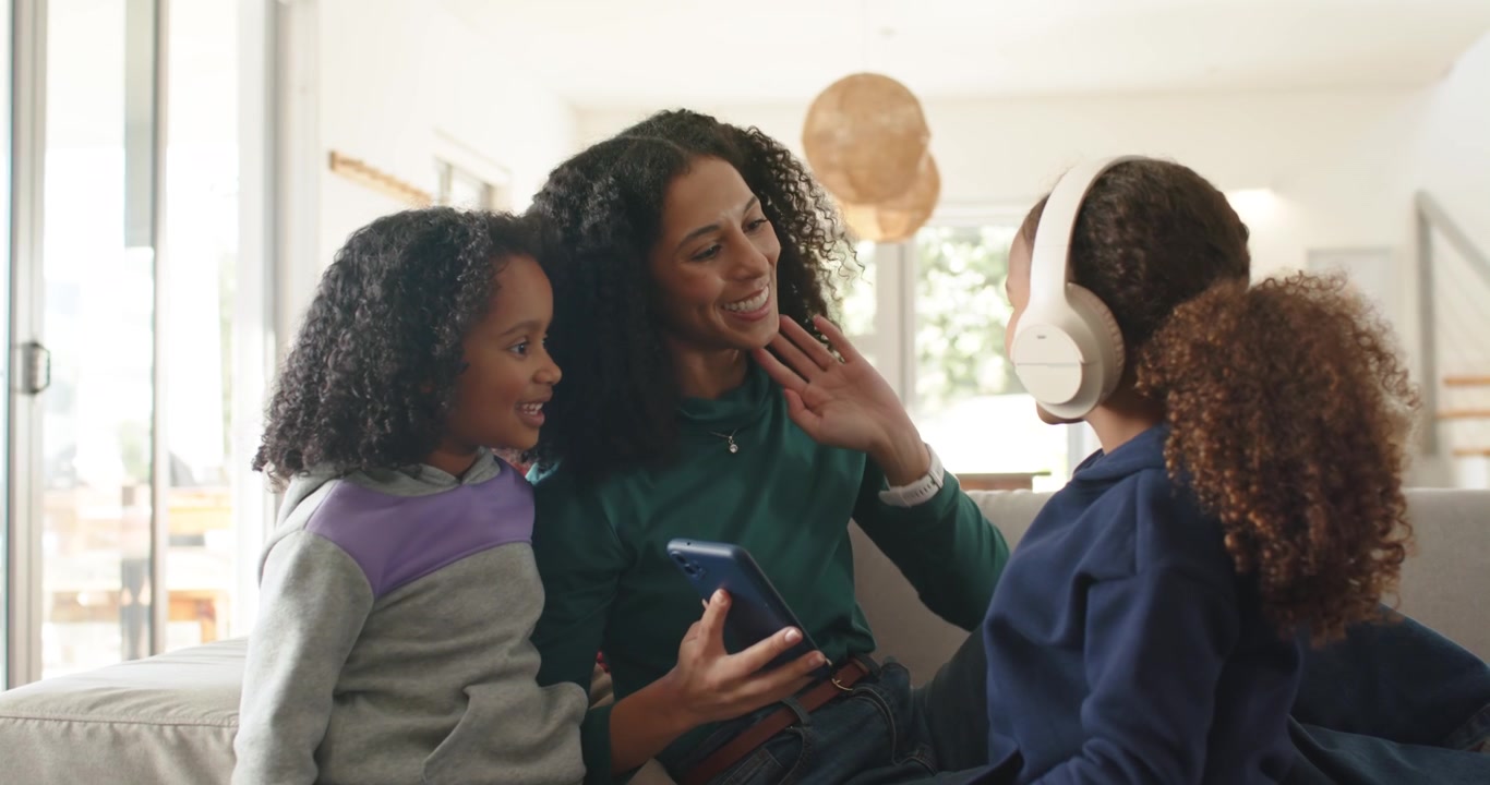 African American mom sharing phone music with daughters at home girls wearing headset and reacting