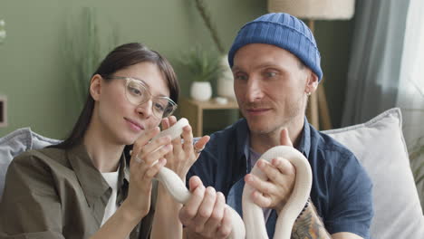 close up view of couple holding a snake and talking together while sitting on a comfortable sofa at home