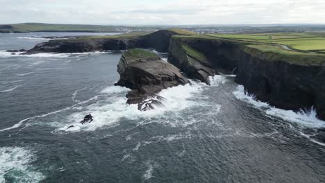 Cliffside-view-of-Kilkee-cliffs-in-Ireland-with-waves-crashing-against-the-rocks,-cloudy-skies-above