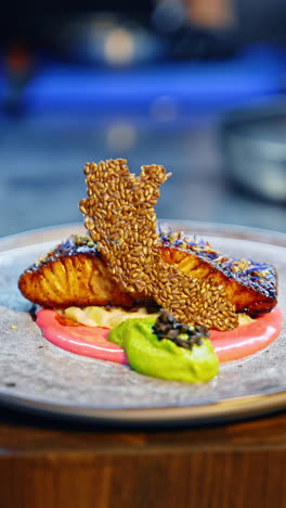 a beautiful dish of fried salmon with two sauces. cook's hand puts the chips made of sesame seeds on the plate. close up. blurred backdrop. vertical video.