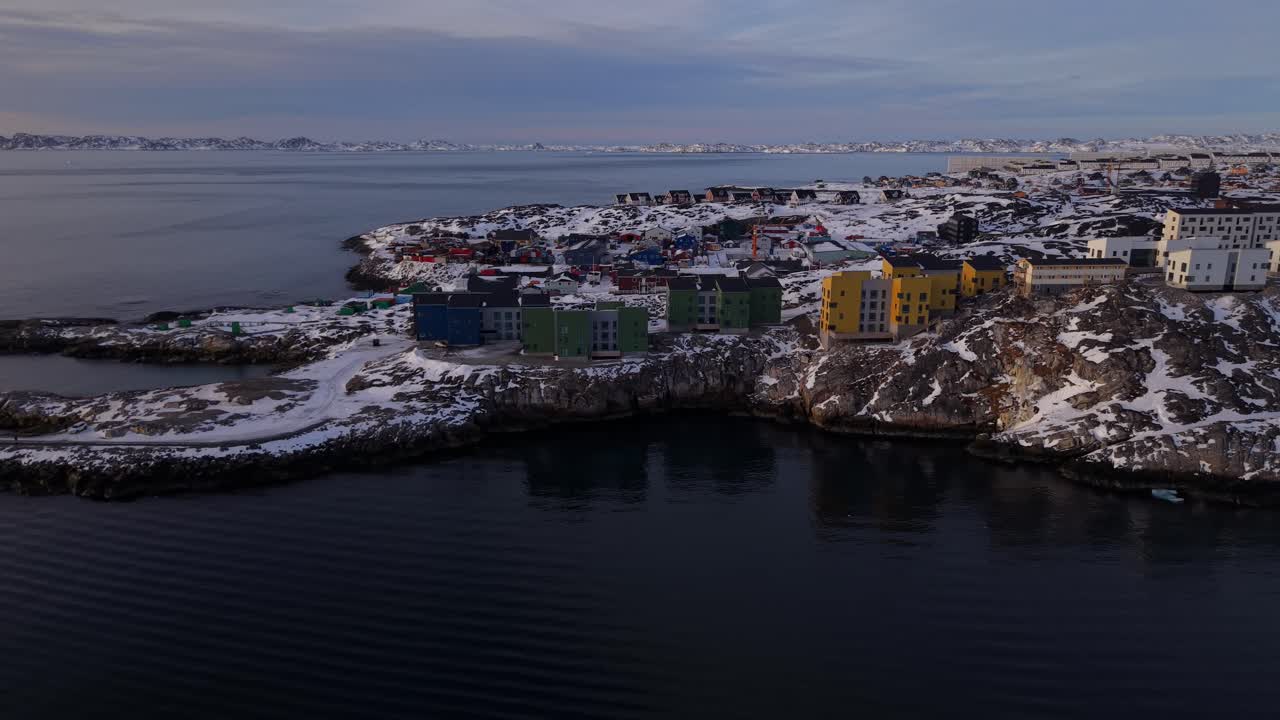 Nuuk'un kayalık kıyılarında geleneksel ve modern renkli evler yer alıyor. Altın saat ışığı karlı manzarayı ve sakin fiyort sularını aydınlatıyor.
