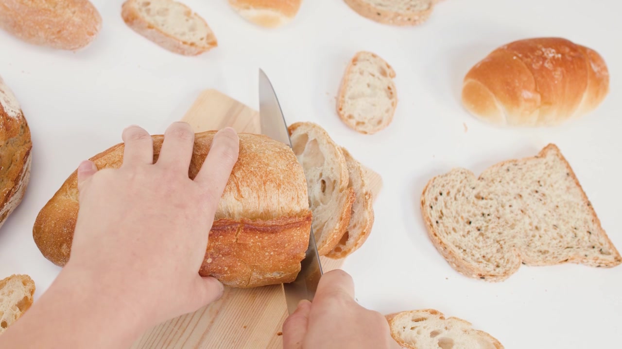 Top-down view of hands using a knife to slice crusty sourdough bread on wood.