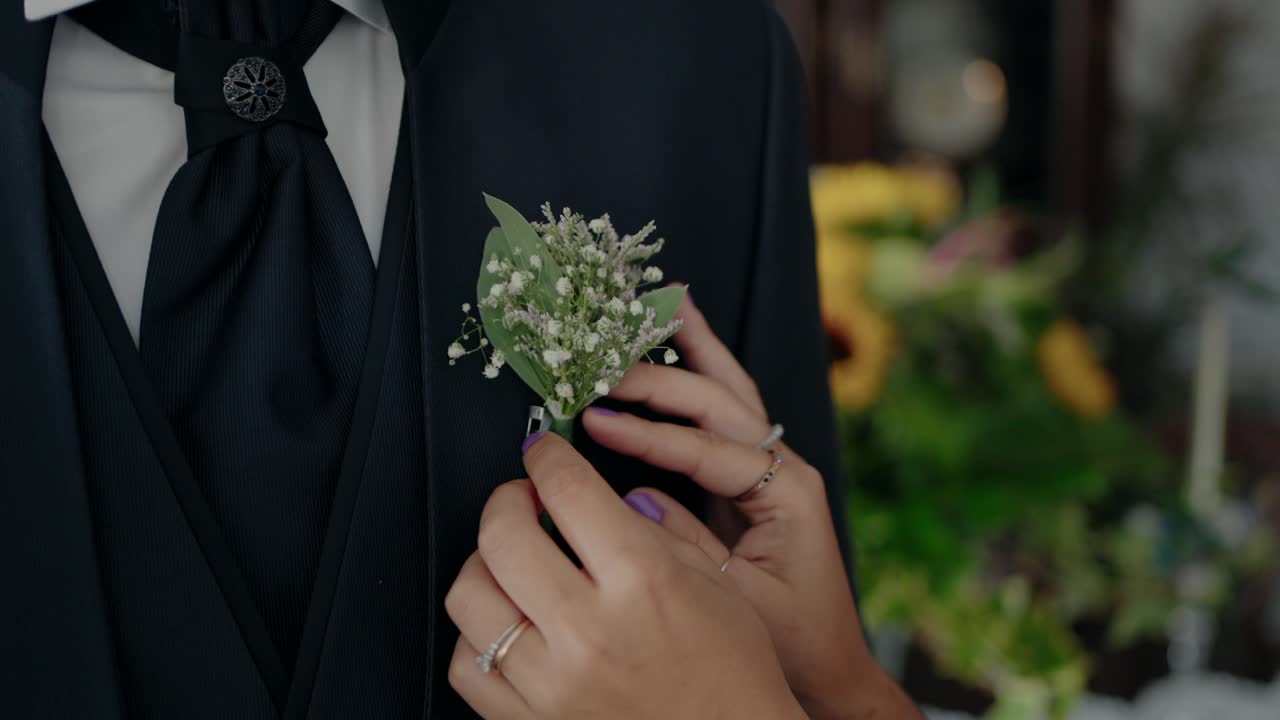 Woman’s hands pinning a delicate floral boutonniere on the groom’s suit lapel
